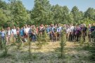 Ein Gruppenfoto mit vielen Menschen in einem lichten Waldstück, im Vordergrund in Reihen gepflanzte kleine Bäume