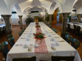 Gewölbesaal mit großem Tisch, gedeckt mit weißem Tischtuch und Blumen in der Mitte