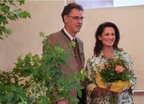 Ein Mann und eine Frau stehen in einem Saal, die Frau hält einen Blumenstrauß in den Händen