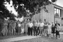 Viele Menschen stehen vor einem Holzhaus, das Foto ist in schwarz-weiß aufgenommen