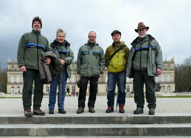 5 Männer und eine Frau stehen mit warmer Kleidung auf der obersten Stufe einer breiten Treppe, im Hintergrund das Schloss Herrenchiemsee